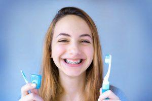 young girl with braces holding toothbrush and floss